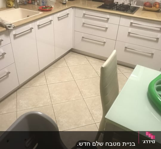 מטבח עם ארונות לבנים, כיור ושולחן זכוכית